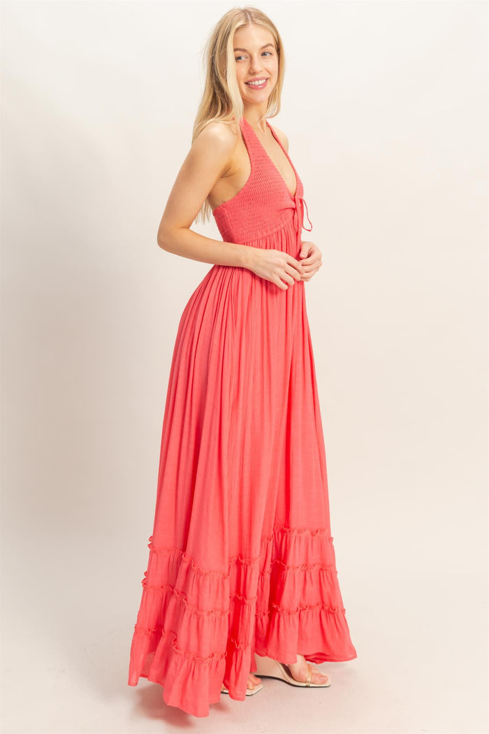 woman wearing a coral halter neck maxi dress with a smocked bodice and tiered ruffle hem