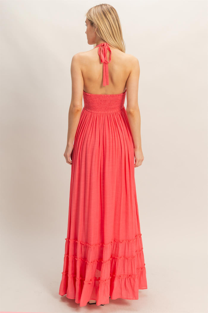 woman wearing a backless coral maxi dress with a smocked bodice and tiered ruffle hem