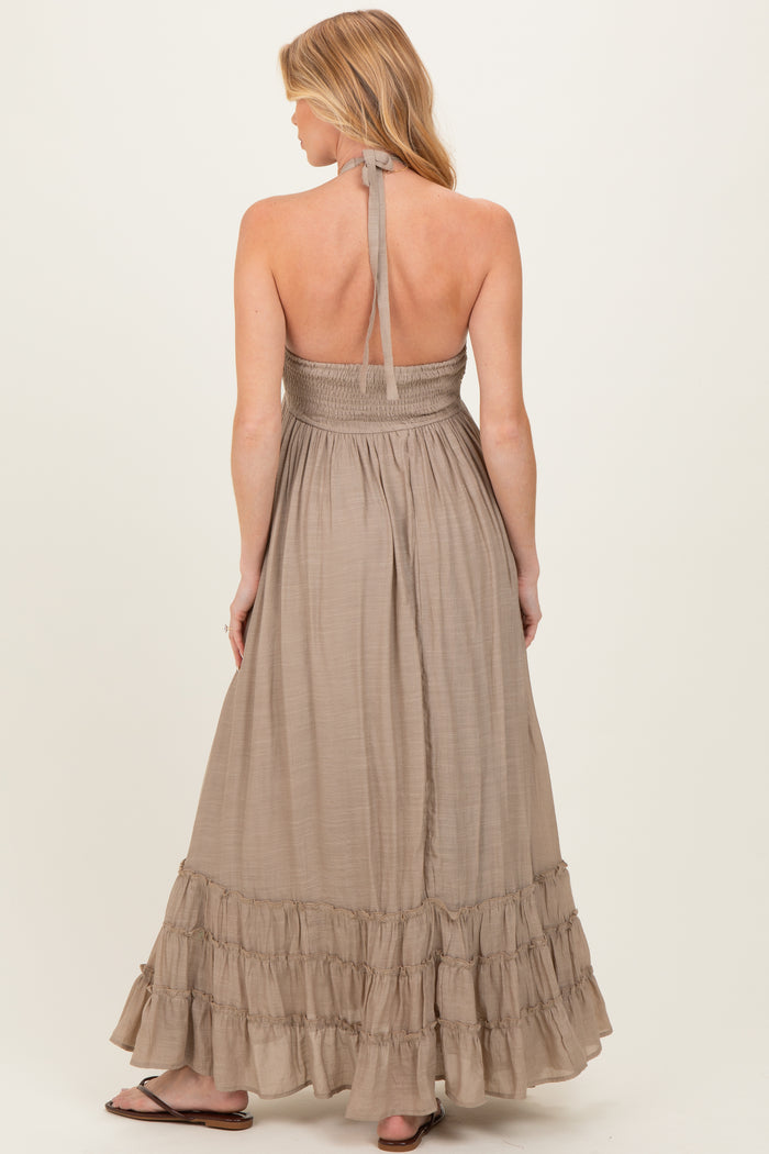 woman wearing a beige halter-style maternity dress with a smocked bodice and a ruffled hem, showing a baby bump