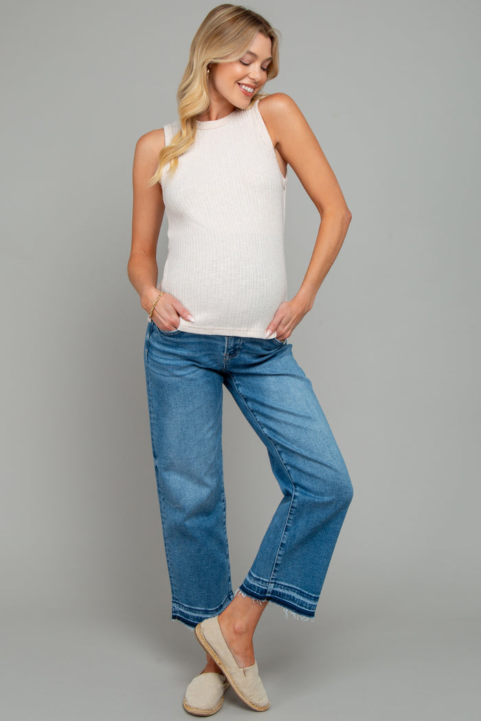 woman wearing a light beige ribbed maternity tank top and blue cropped jeans, showing her baby bump