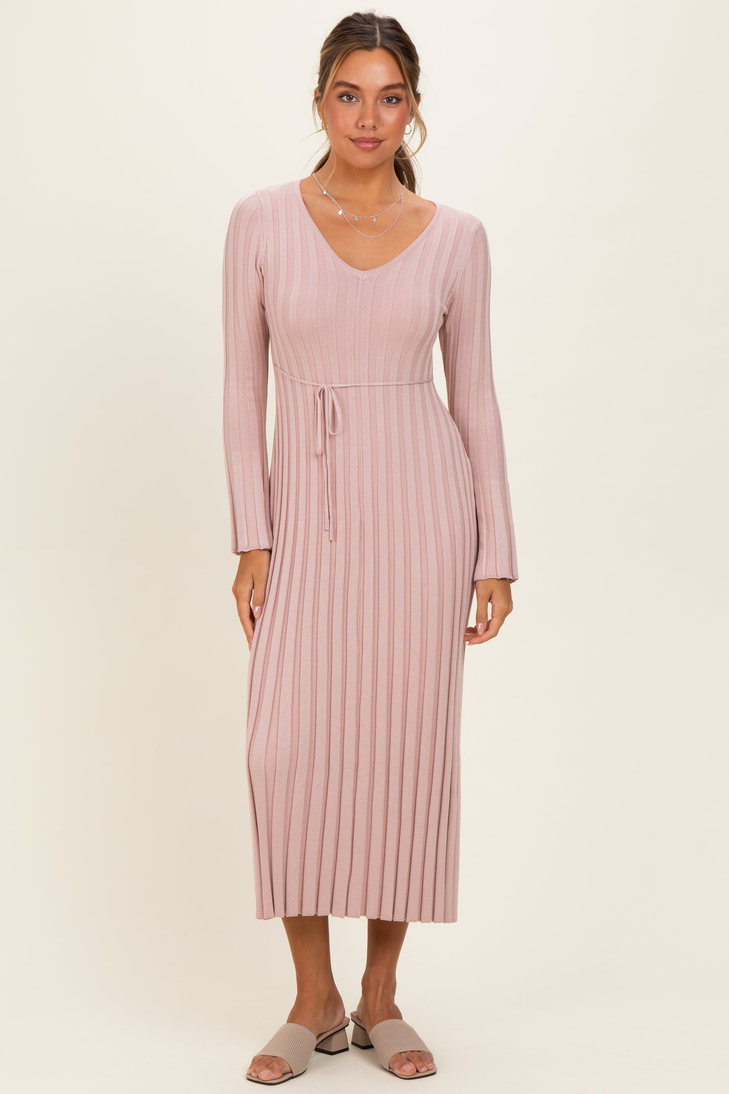 woman wearing a light pink ribbed long sleeve dress with a v-neck and a tie waist detail