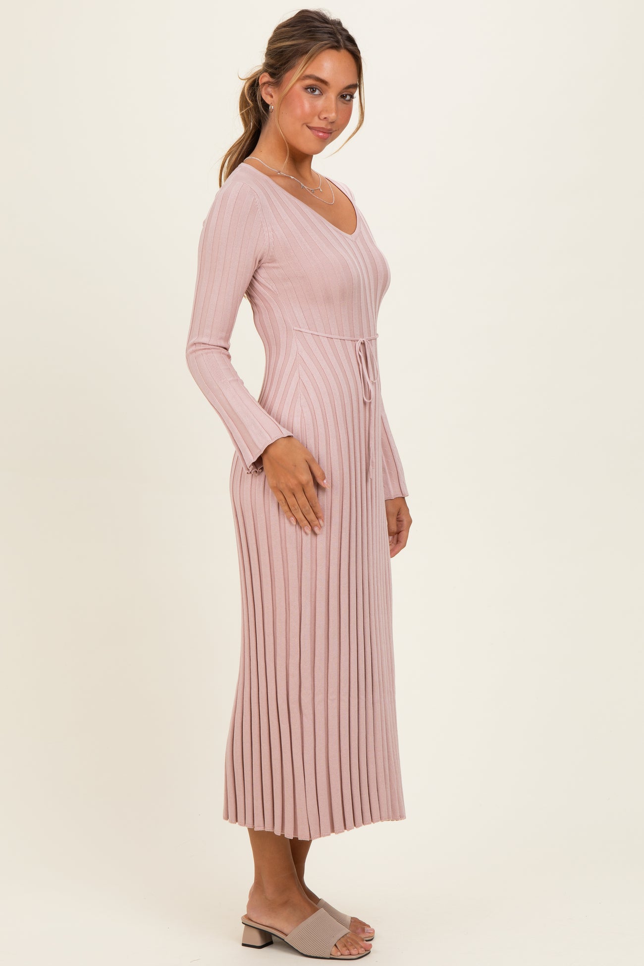 woman wearing a long sleeve ribbed pink dress with a drawstring waist and side slits, standing against a neutral background