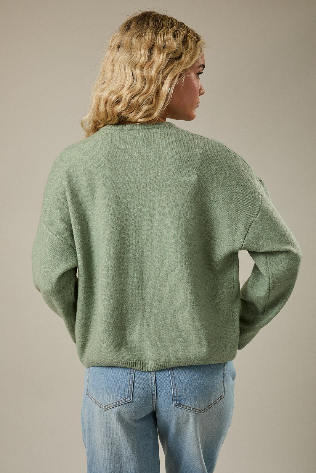 woman wearing a light green oversized sweater with long sleeves and back-facing view paired with light blue jeans