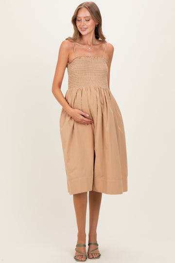 woman wearing a beige maternity dress with a smocked bodice and flowy skirt, holding her baby bump