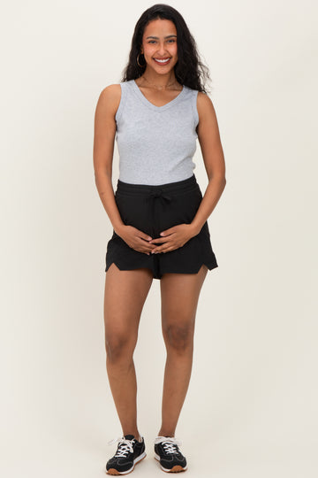 woman wearing a gray sleeveless top and black maternity shorts, holding her baby bump