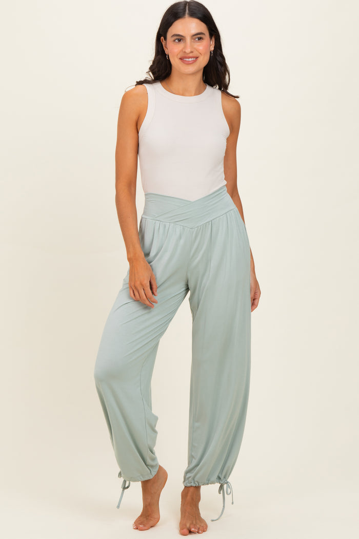 woman wearing a light gray sleeveless top and mint green high-waisted pants with adjustable cuffs.