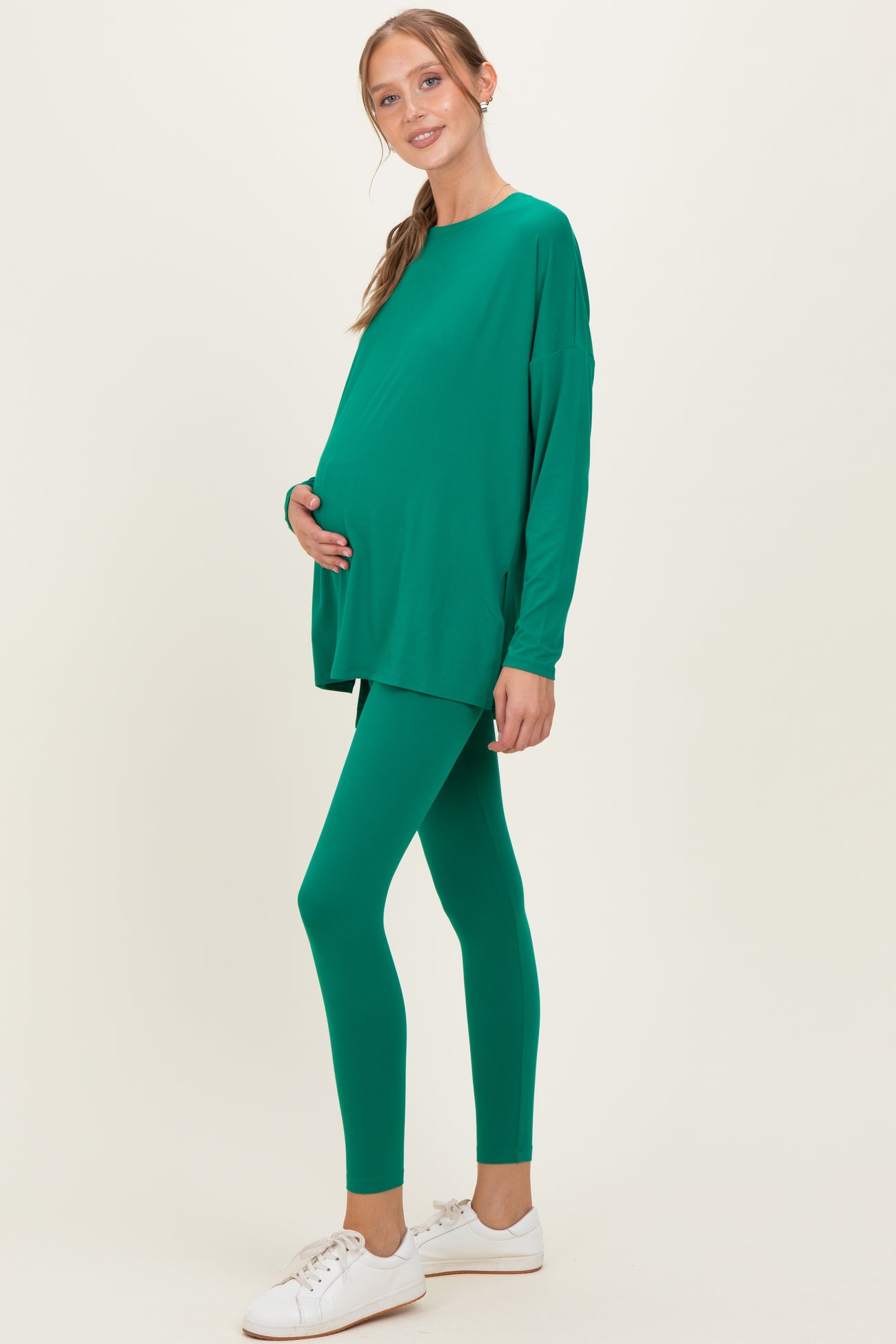 woman wearing a green long sleeve maternity top and matching leggings, holding her baby bump