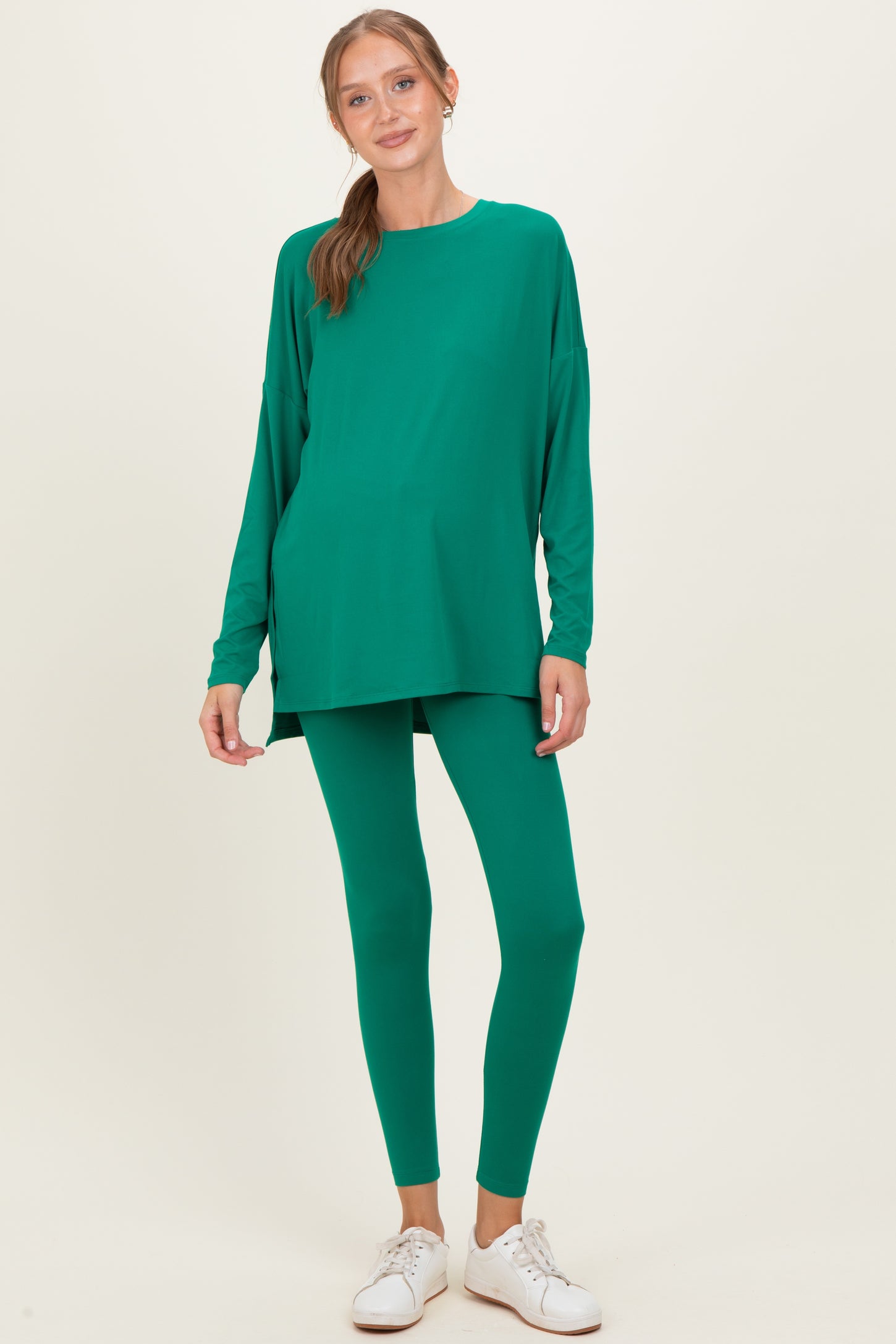 woman wearing a green maternity top and matching leggings, showing a visible baby bump, styled with white sneakers