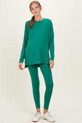 woman wearing a green maternity top and matching leggings, showing a visible baby bump, styled with white sneakers