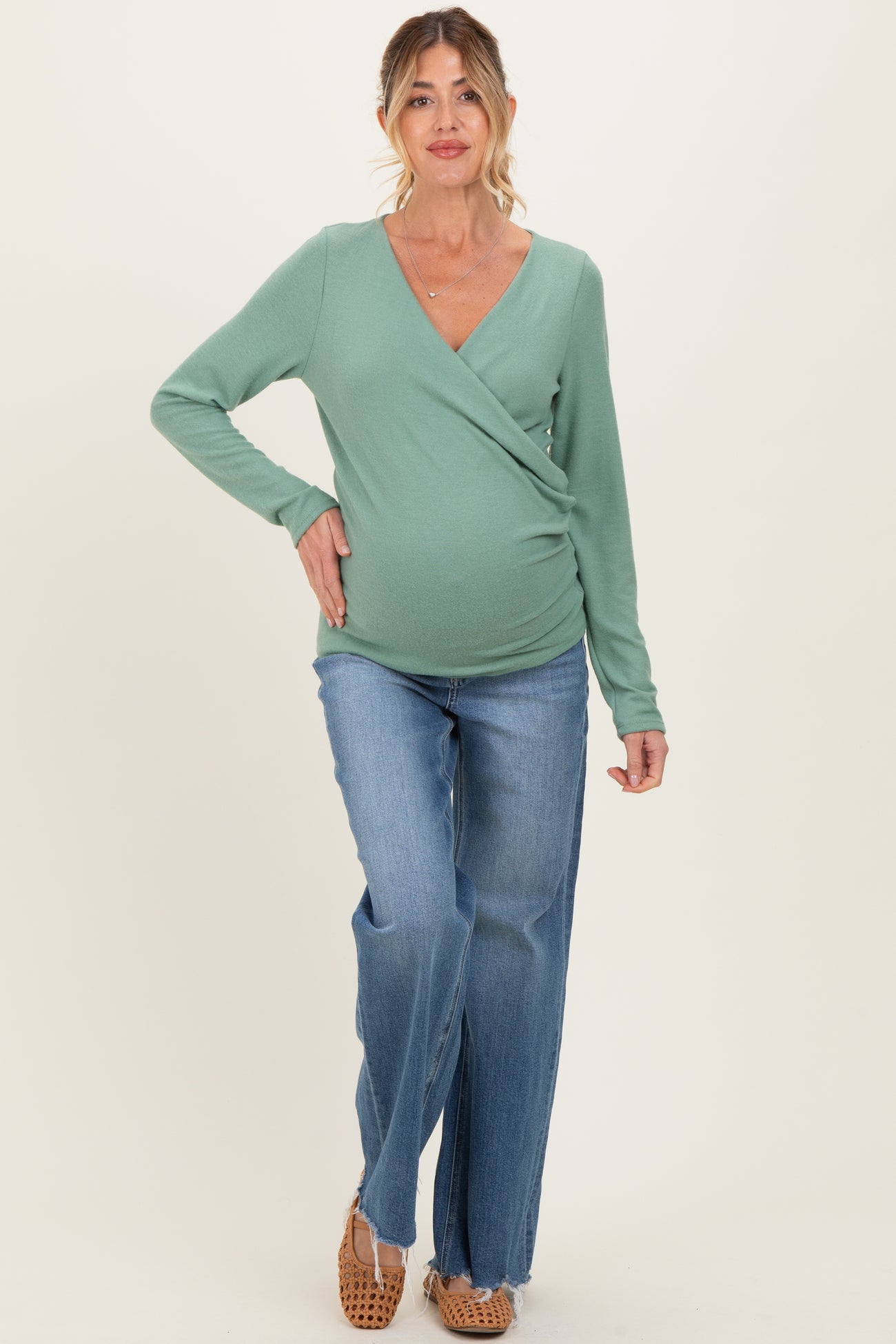 woman wearing a green long sleeve wrap maternity top and blue jeans, showing her baby bump