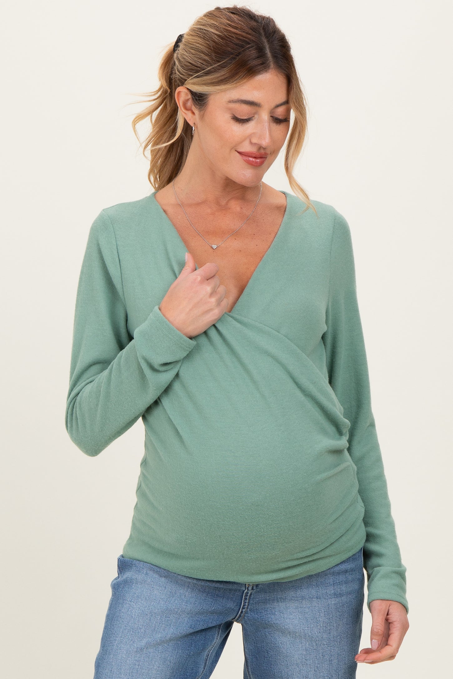 woman wearing a green maternity wrap top and showing her baby bump with a relaxed smile