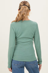 woman wearing a green long sleeve maternity top, view from the back, paired with blue jeans