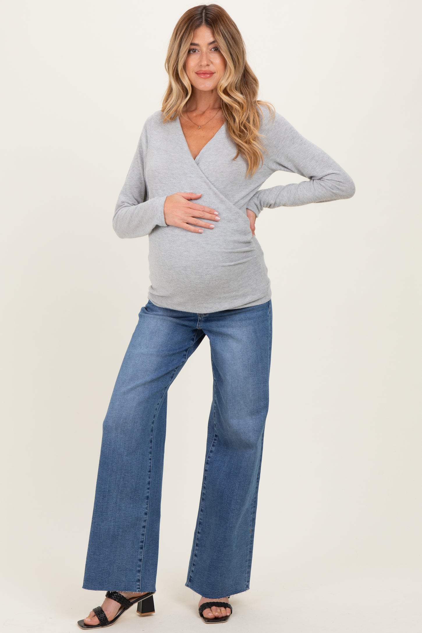 woman wearing a gray long sleeve maternity wrap top and blue wide leg jeans, showing her baby bump