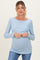 woman wearing a light blue long sleeve maternity top and holding her baby bump