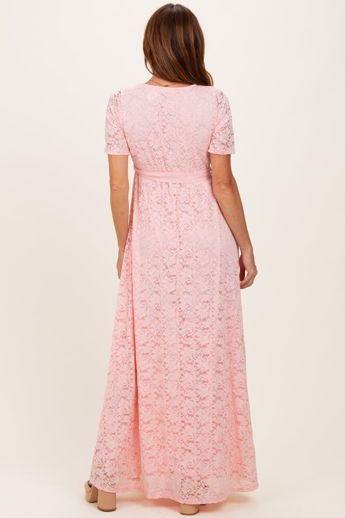 woman wearing a pink lace maxi dress with short sleeves and a tied waist detail, shown from the back