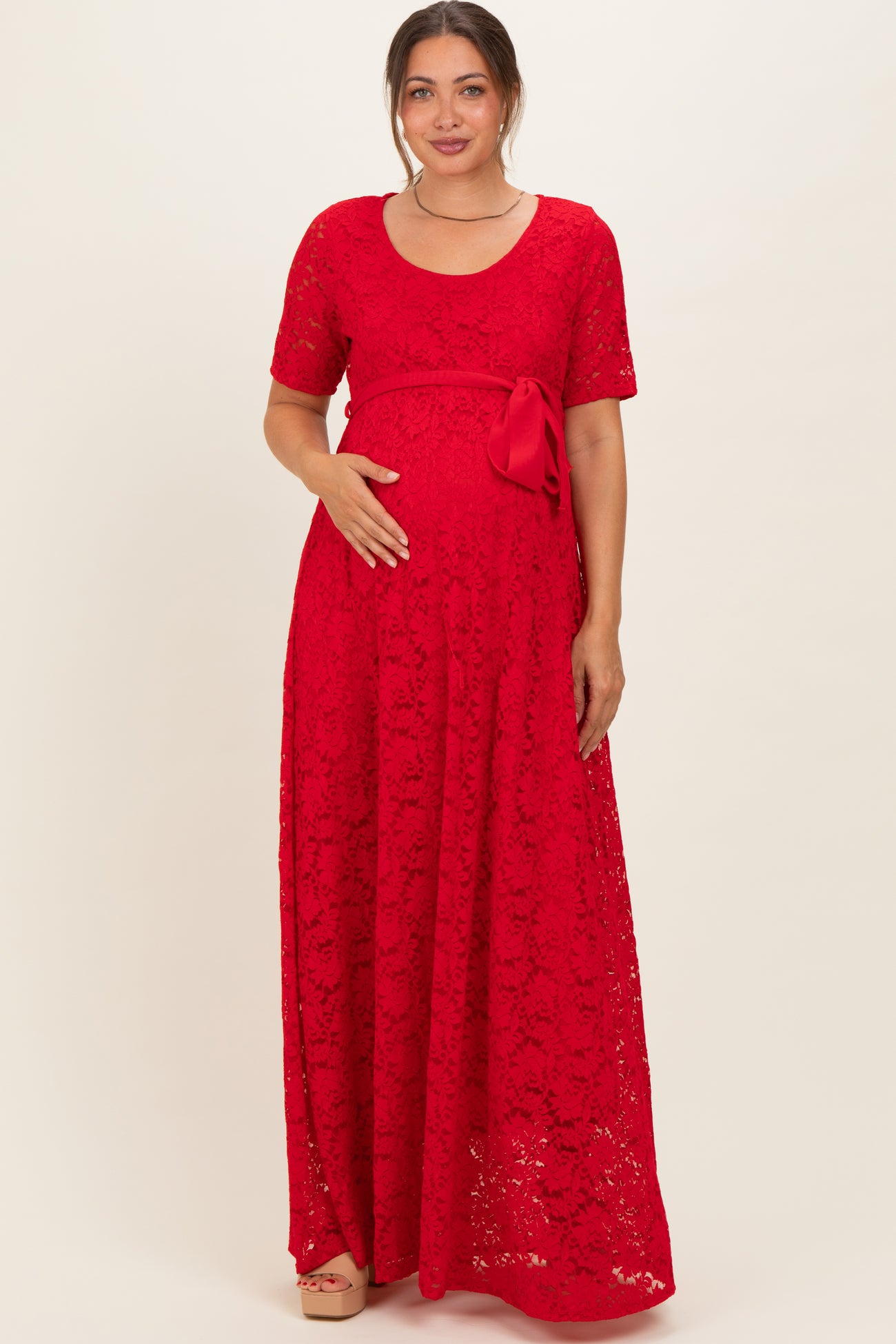 woman wearing a red lace maxi maternity dress with a bow detail and holding her baby bump