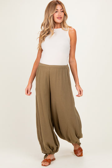 woman wearing a cream tank top and olive green maternity wide-leg pants, walking with a casual pose
