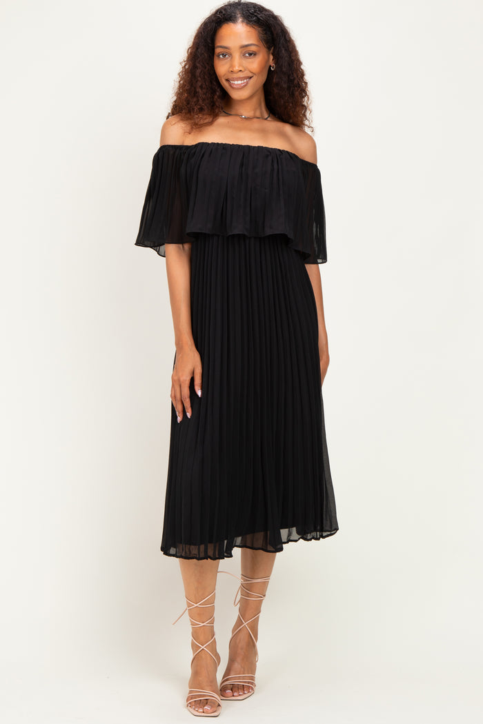 woman wearing a black off-the-shoulder pleated dress with a flowing ruffle detail and strappy sandals
