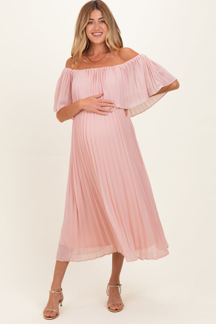 woman wearing a pink off-the-shoulder pleated maternity dress and holding her baby bump
