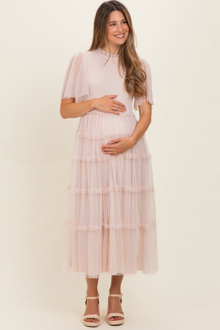 woman wearing a light pink tiered tulle maternity dress and showing her baby bump