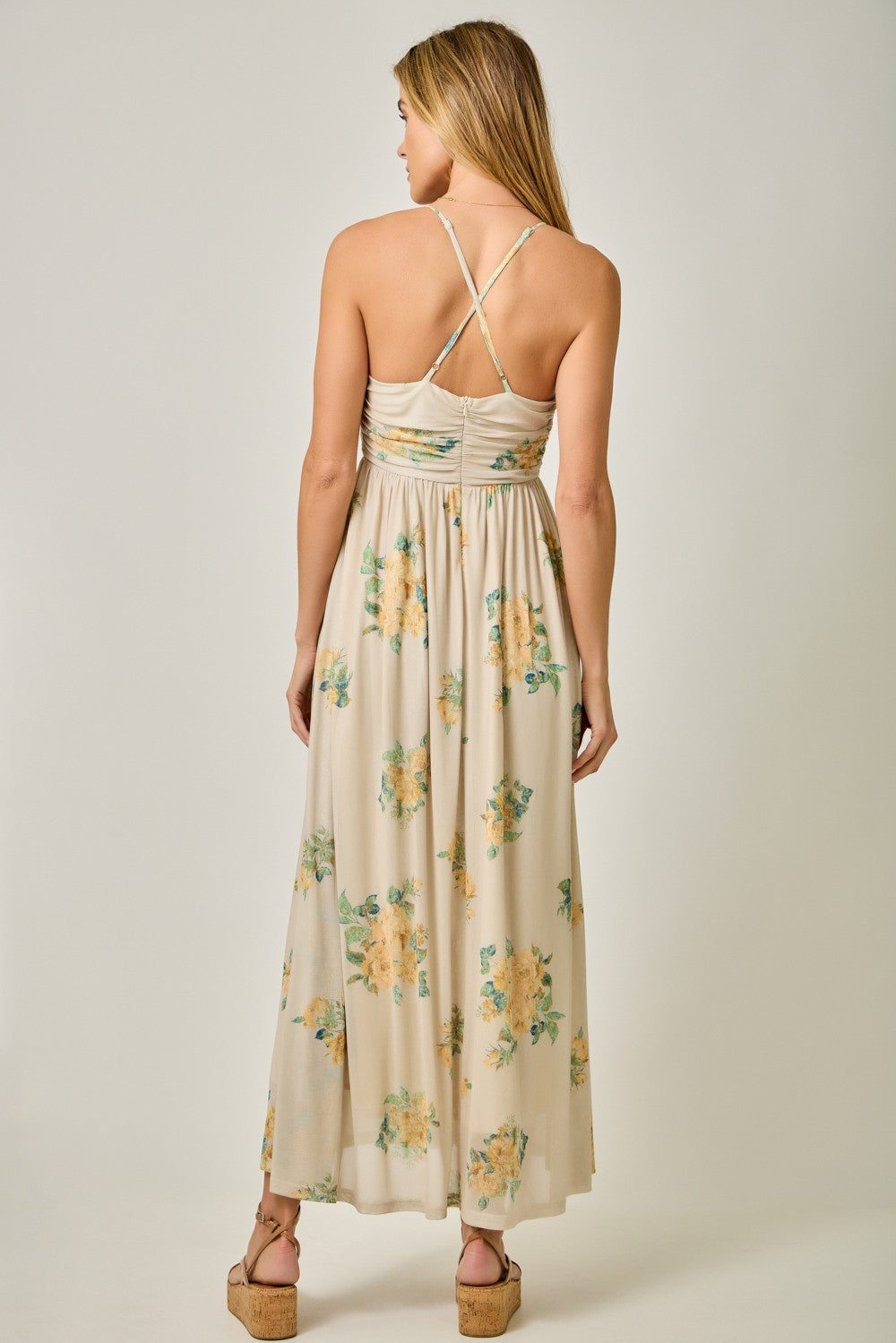 woman wearing a floral maxi dress with a low back and crisscross straps, showing a relaxed fit and flowy fabric
