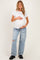 woman wearing a white short sleeve maternity top and ripped light wash jeans, holding her baby bump