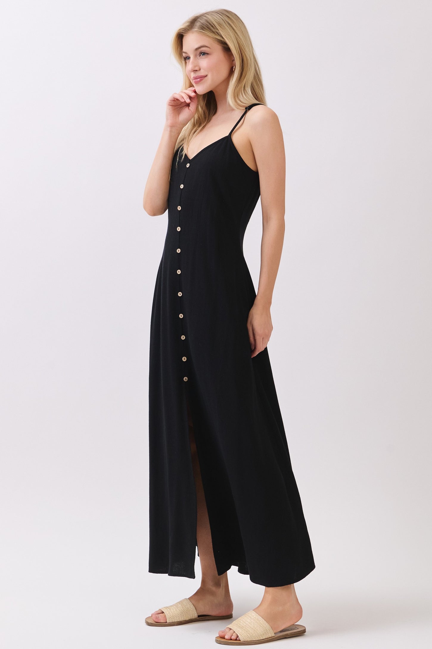 woman wearing a black maxi dress with buttons down the front and thin straps, styled with flat sandals