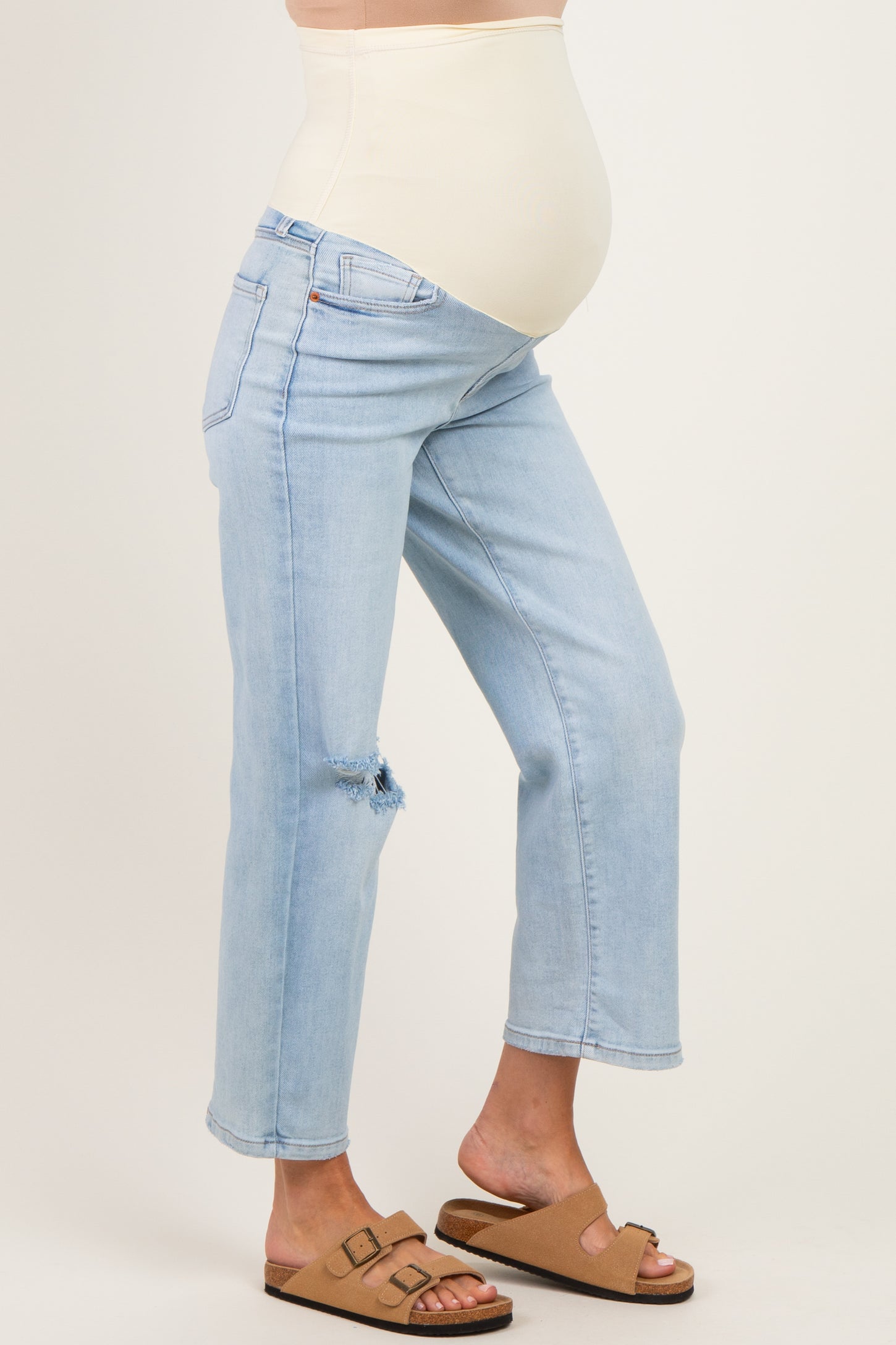 woman wearing light blue maternity jeans with a distressed knee and a beige belly panel, showing her baby bump
