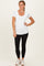 woman wearing a white short sleeve scoop neck top and black leggings, standing with hands on hips