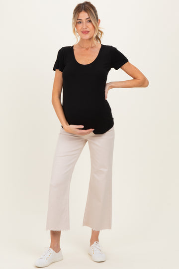 woman wearing a black scoop neck maternity top and holding her baby bump, paired with light beige cropped pants and white sneakers