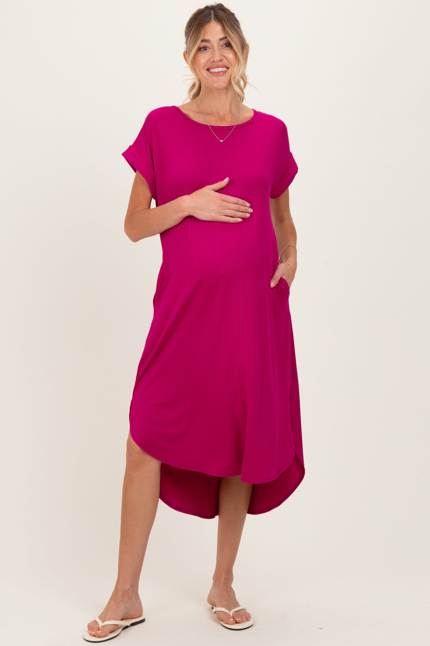 woman wearing a hot pink maternity dress with short sleeves and a high-low hem, holding her baby bump