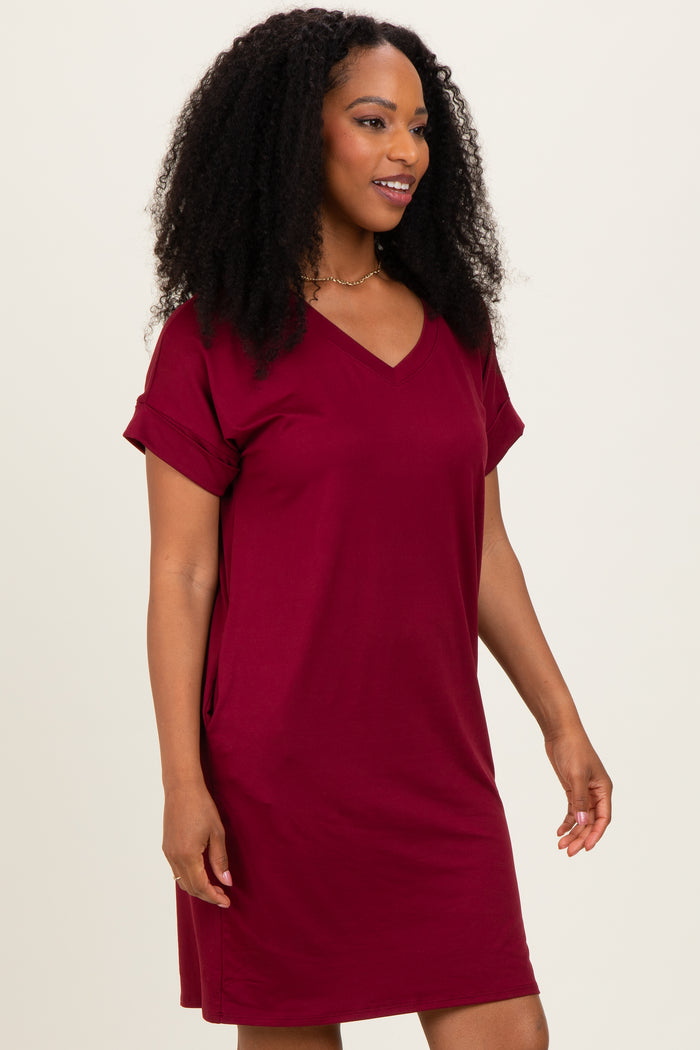 woman wearing a burgundy short sleeve v-neck dress with rolled sleeves and side pockets