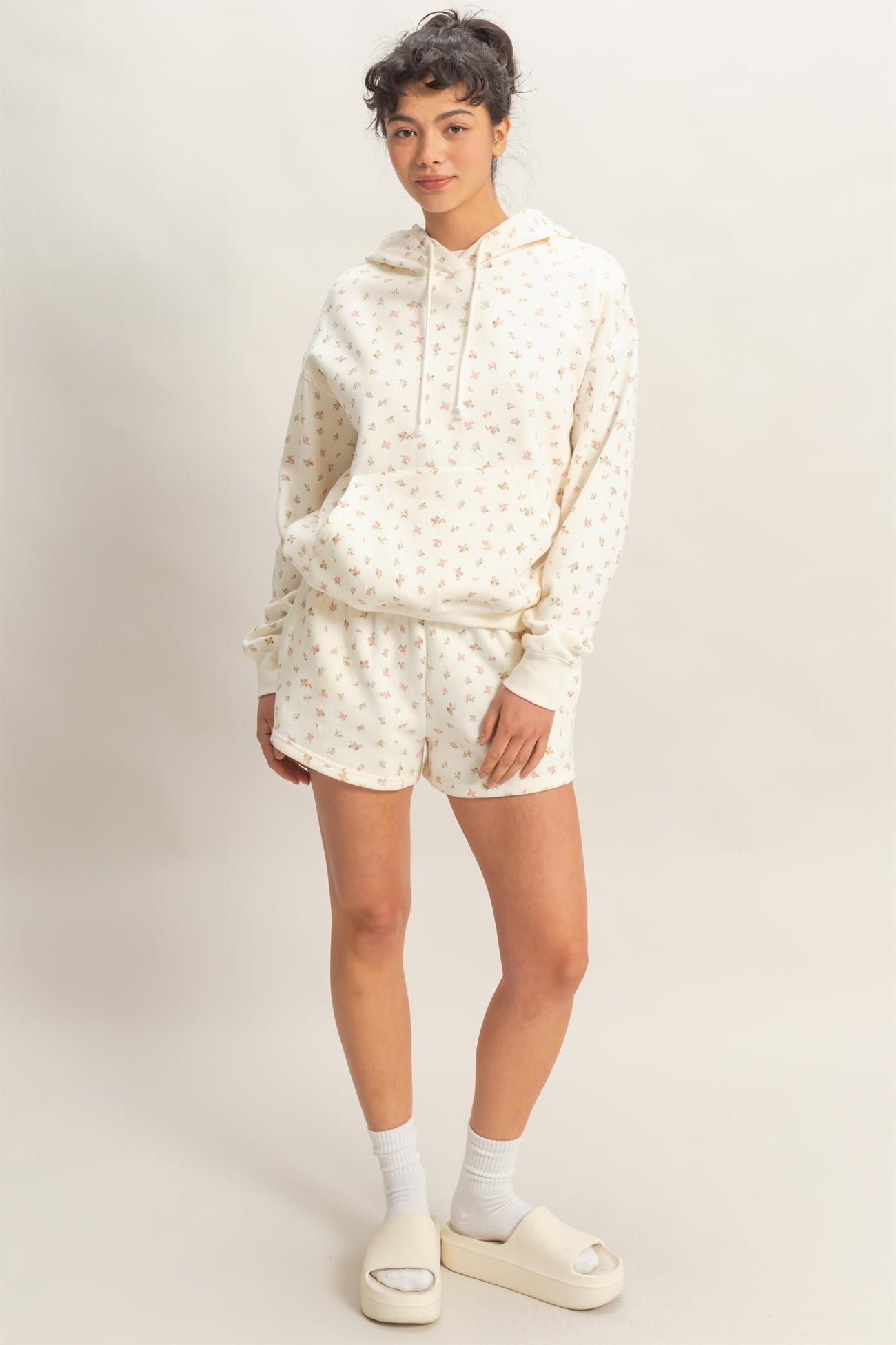 woman wearing a cream hoodie with floral print and matching shorts, styled with white socks and slide sandals