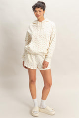 woman wearing a cream hoodie with floral print and matching shorts, styled with white socks and slide sandals