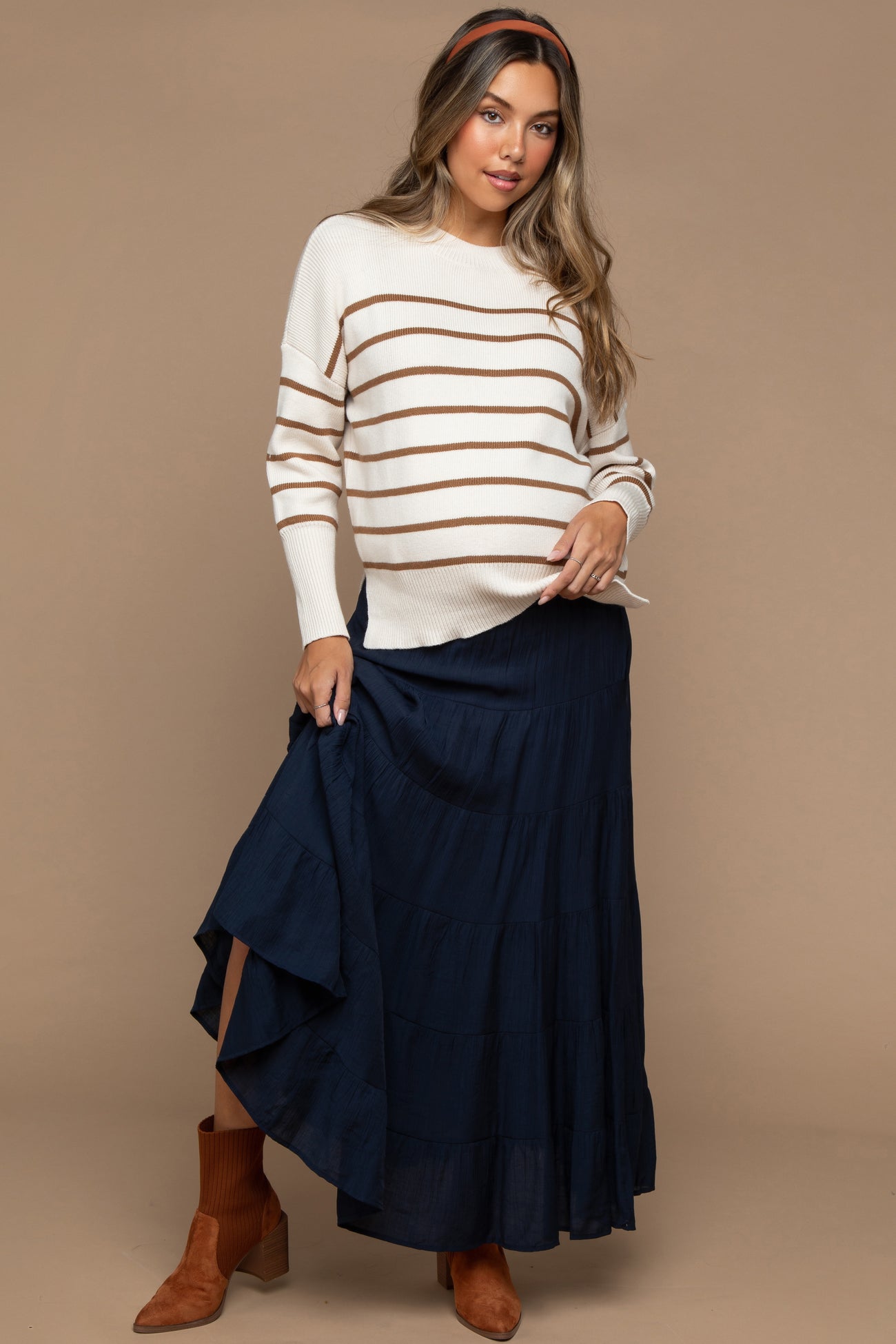 woman wearing a cream and brown striped maternity sweater and a navy maxi skirt, showing her baby bump