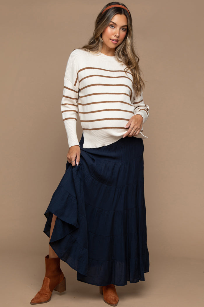 woman wearing a cream and brown striped maternity sweater and a navy maxi skirt, showing her baby bump