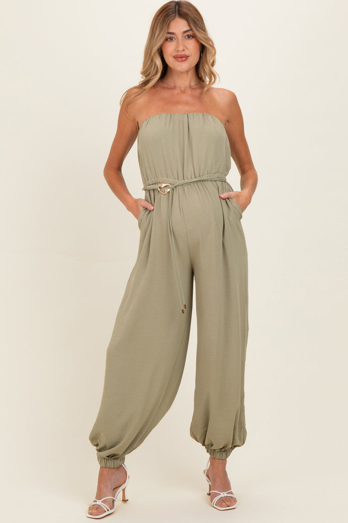 woman wearing a green strapless maternity jumpsuit with a belted waist and side pockets, showing a baby bump