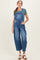 woman wearing a blue denim maternity overall with a green short sleeve top and standing with one hand in the pocket