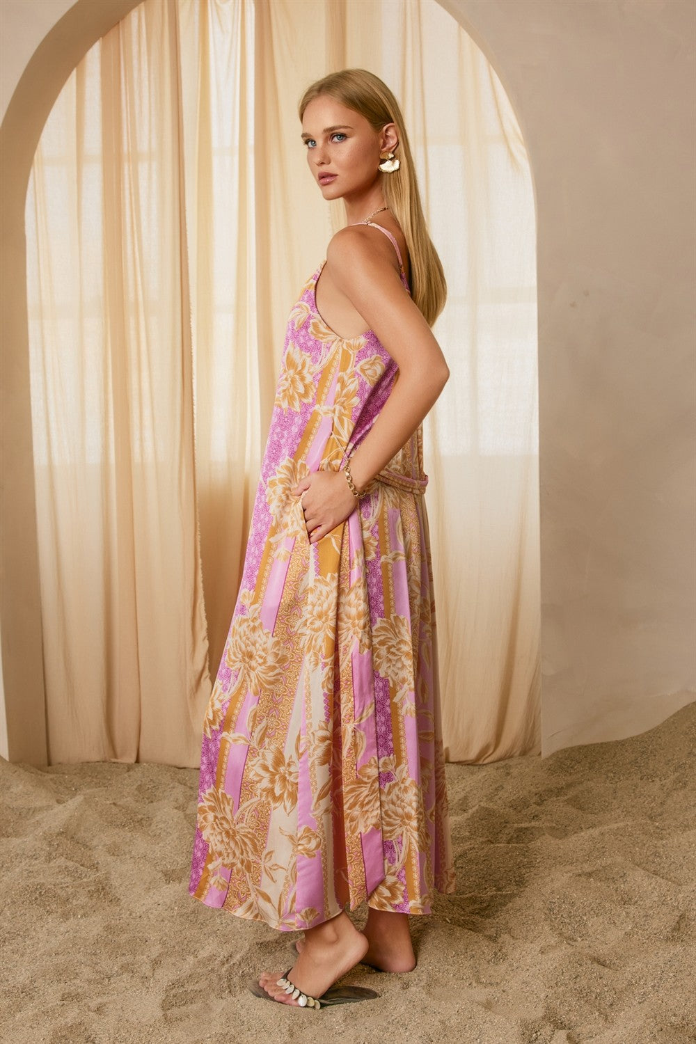 woman wearing a pink and cream floral maxi dress with spaghetti straps, standing against a soft beige backdrop