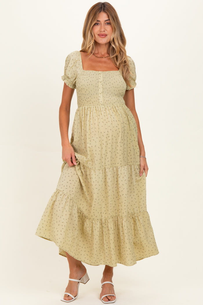 woman wearing a light green floral print maternity dress with a square neckline and puff sleeves, holding her baby bump