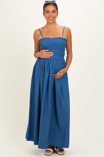 woman wearing a blue maternity maxi dress with a smocked bodice and holding her baby bump
