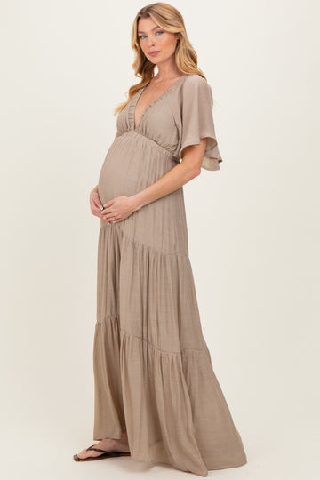 woman wearing a beige tiered maternity dress, holding her baby bump with a flowy silhouette and flutter sleeves