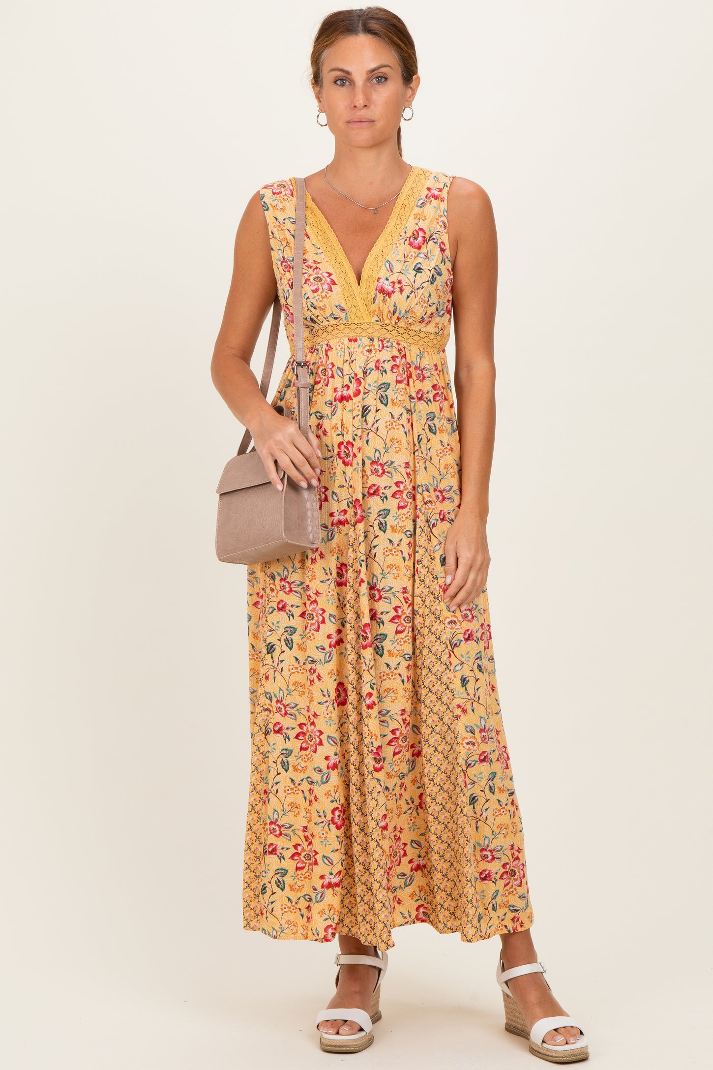 woman wearing a yellow floral maxi dress with a v-neckline and a fitted waist, carrying a small handbag