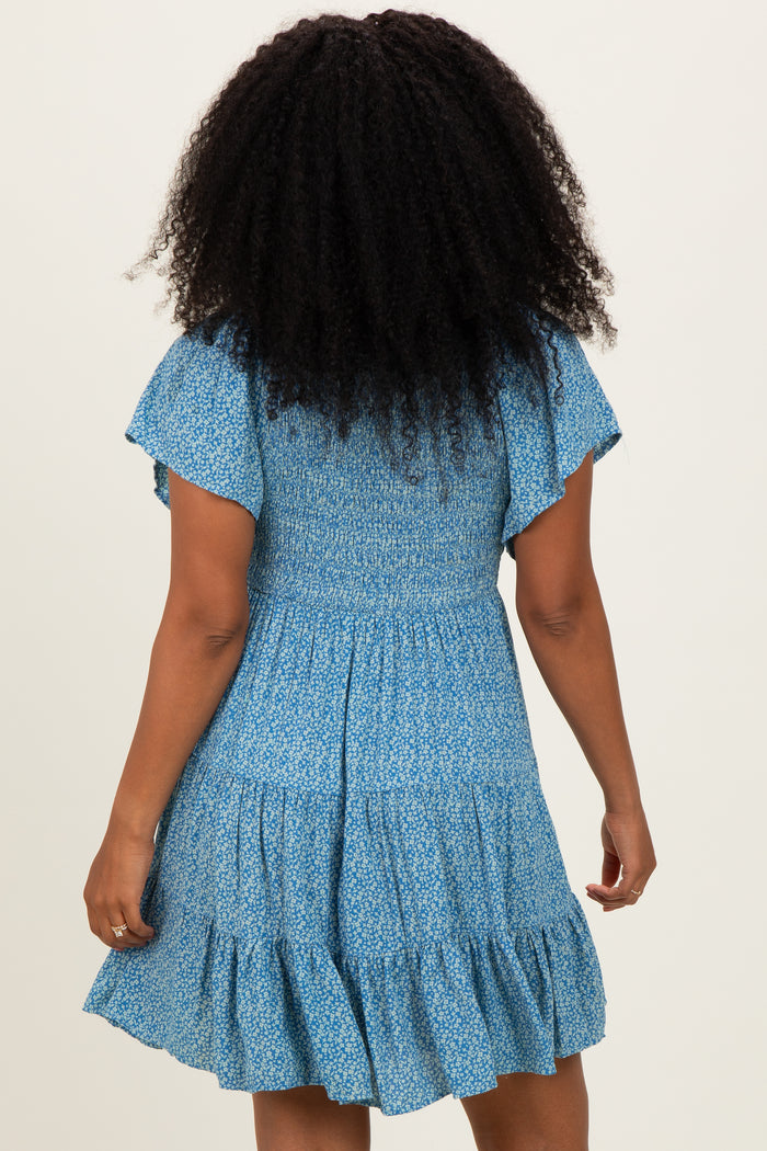 woman wearing a blue floral short sleeve dress with a smocked bodice and tiered ruffle skirt from the back
