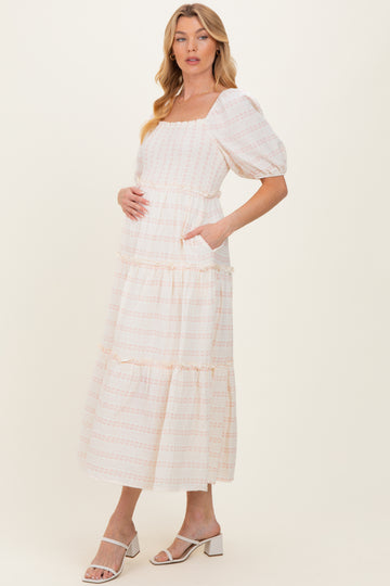 woman wearing a cream maternity maxi dress with square neckline and puff sleeves, holding her baby bump