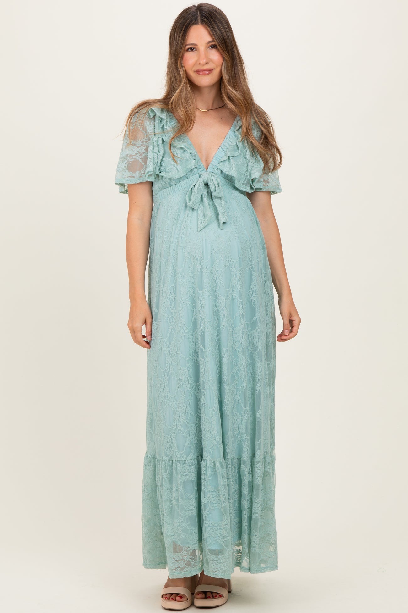 woman wearing a light blue lace maternity dress with short flutter sleeves and a tie front, showcasing her baby bump