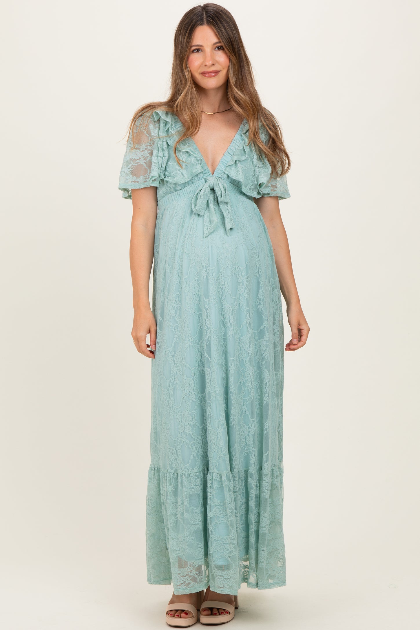 woman wearing a light blue lace maternity dress with short flutter sleeves and a tie front, showcasing her baby bump