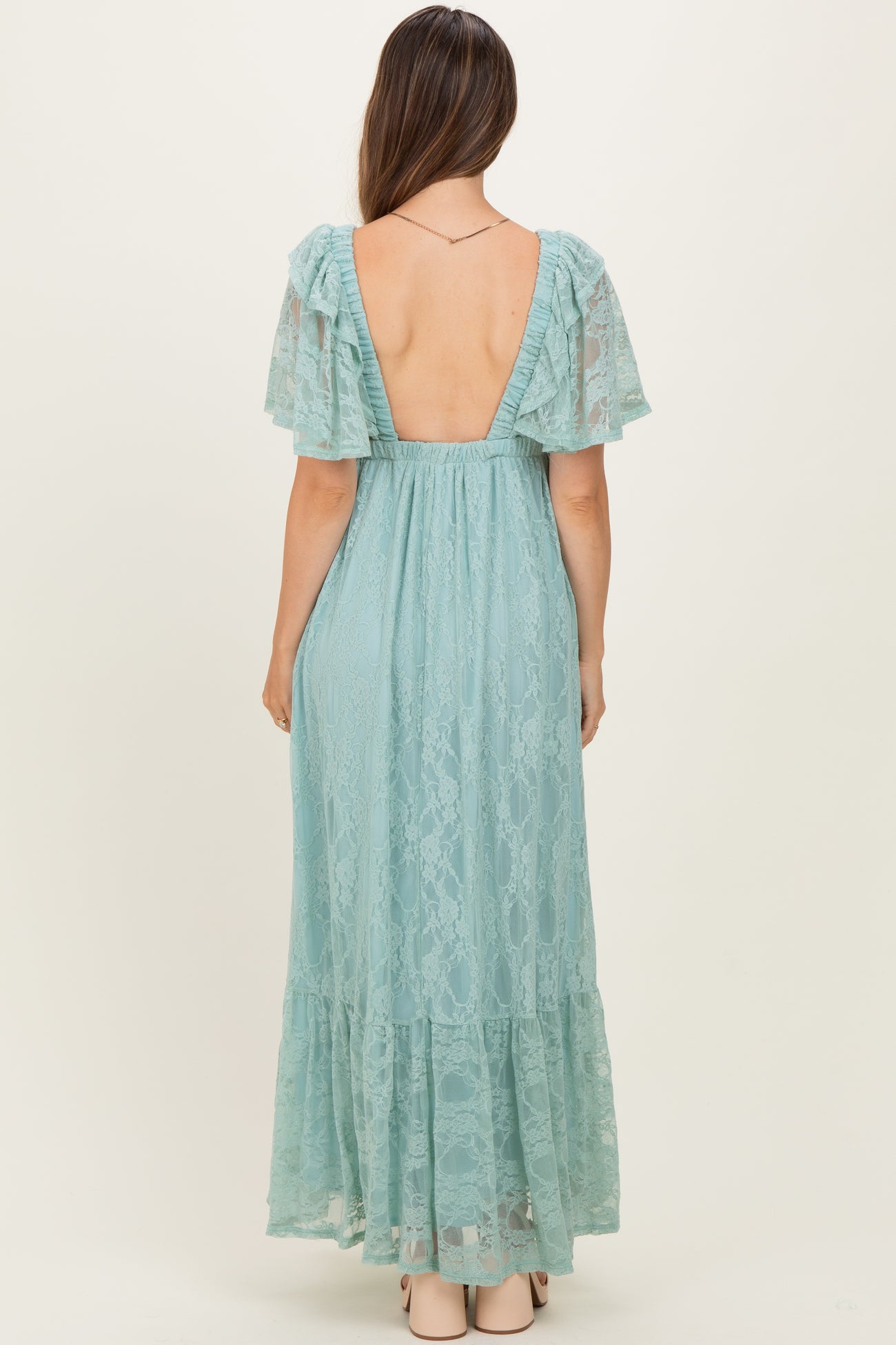 woman wearing a backless light blue lace maternity gown with flutter sleeves and a flowy skirt