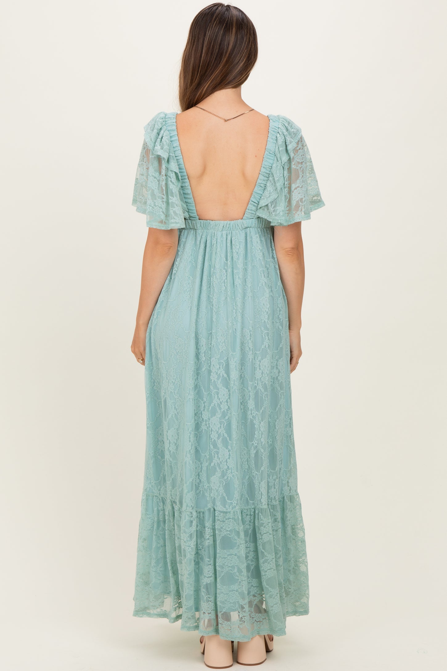woman wearing a backless light blue lace maternity gown with flutter sleeves and a flowy skirt