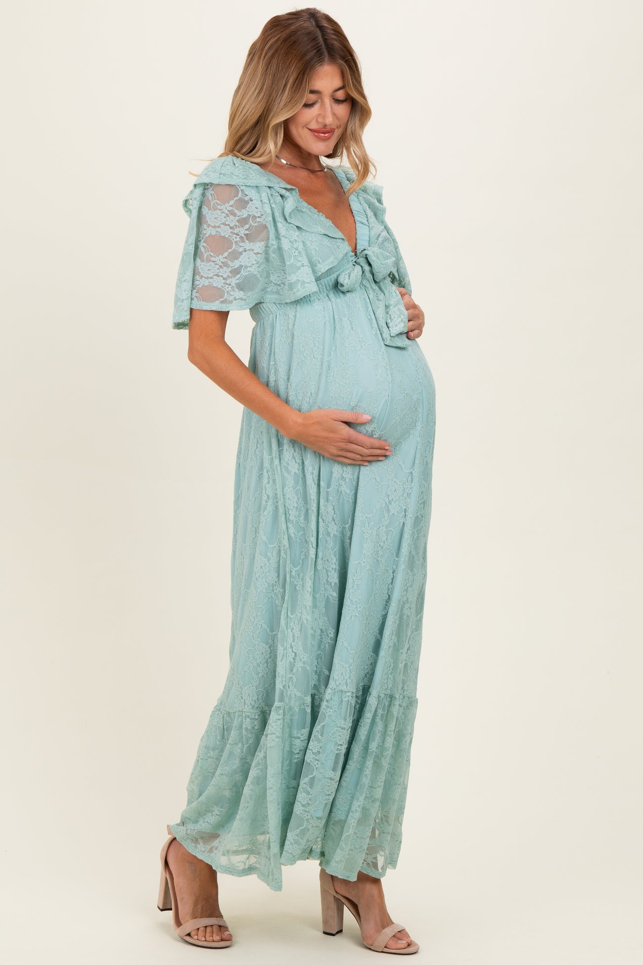 woman wearing a light blue lace maternity maxi dress with ruffled sleeves and a bow, holding her baby bump